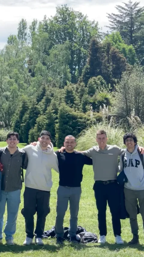 Cinco personas del equipo abrazadas en un parque, rodeadas de árboles