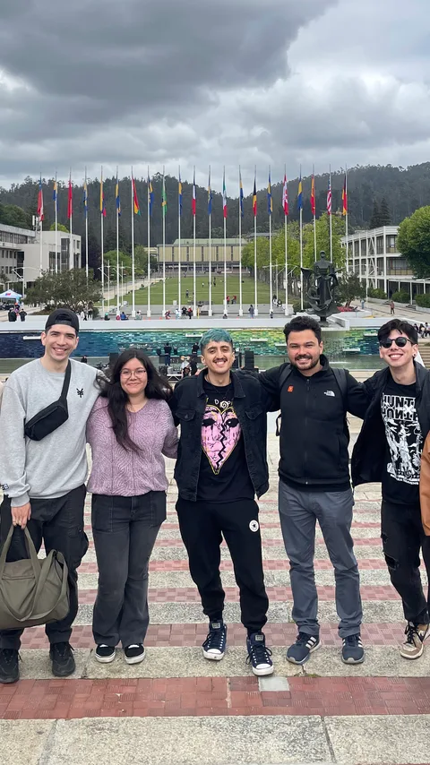 Cinco personas del equipo frente a un campus universitario con banderas