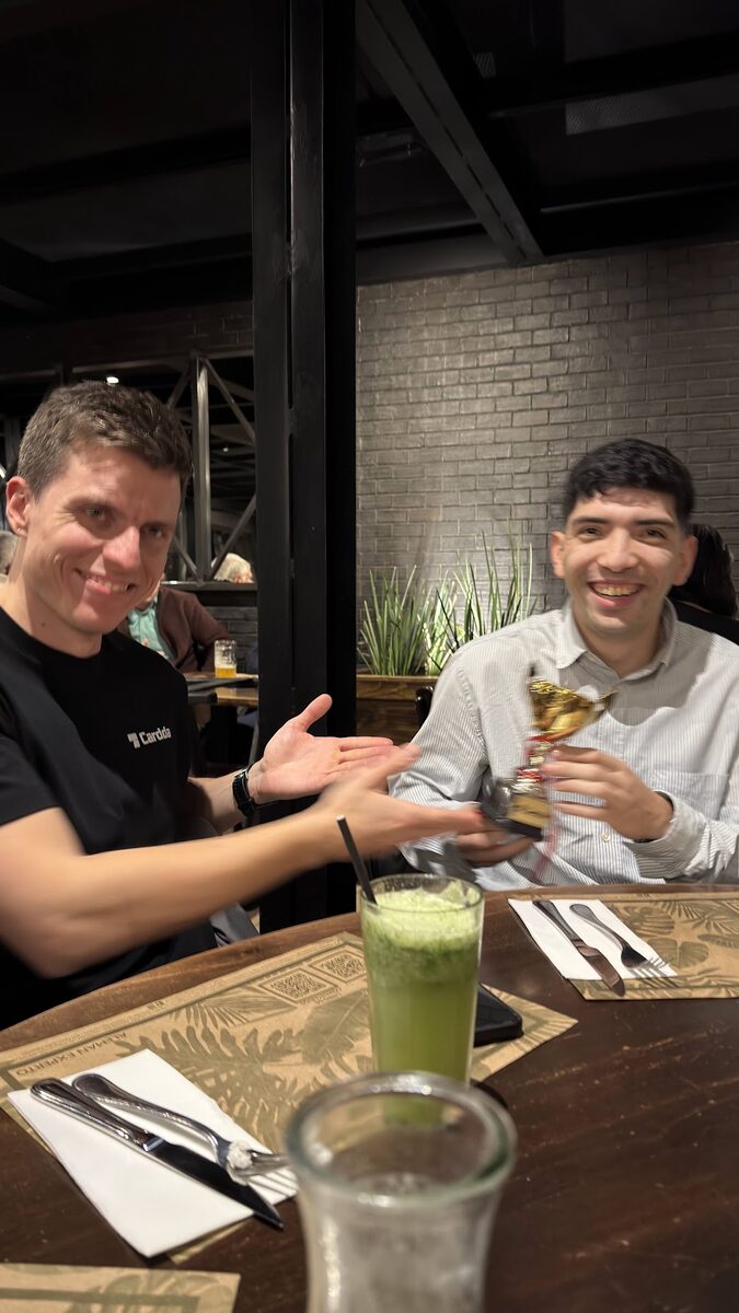 Dos personas del equipo en una mesa, una entregándole un trofeo dorado a la otra